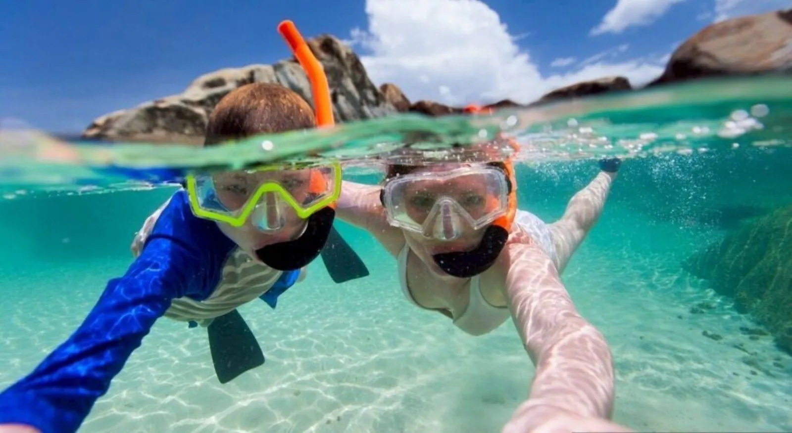 Two snorkellers at the surface in an over-under shot, masks above and fins below the waterline