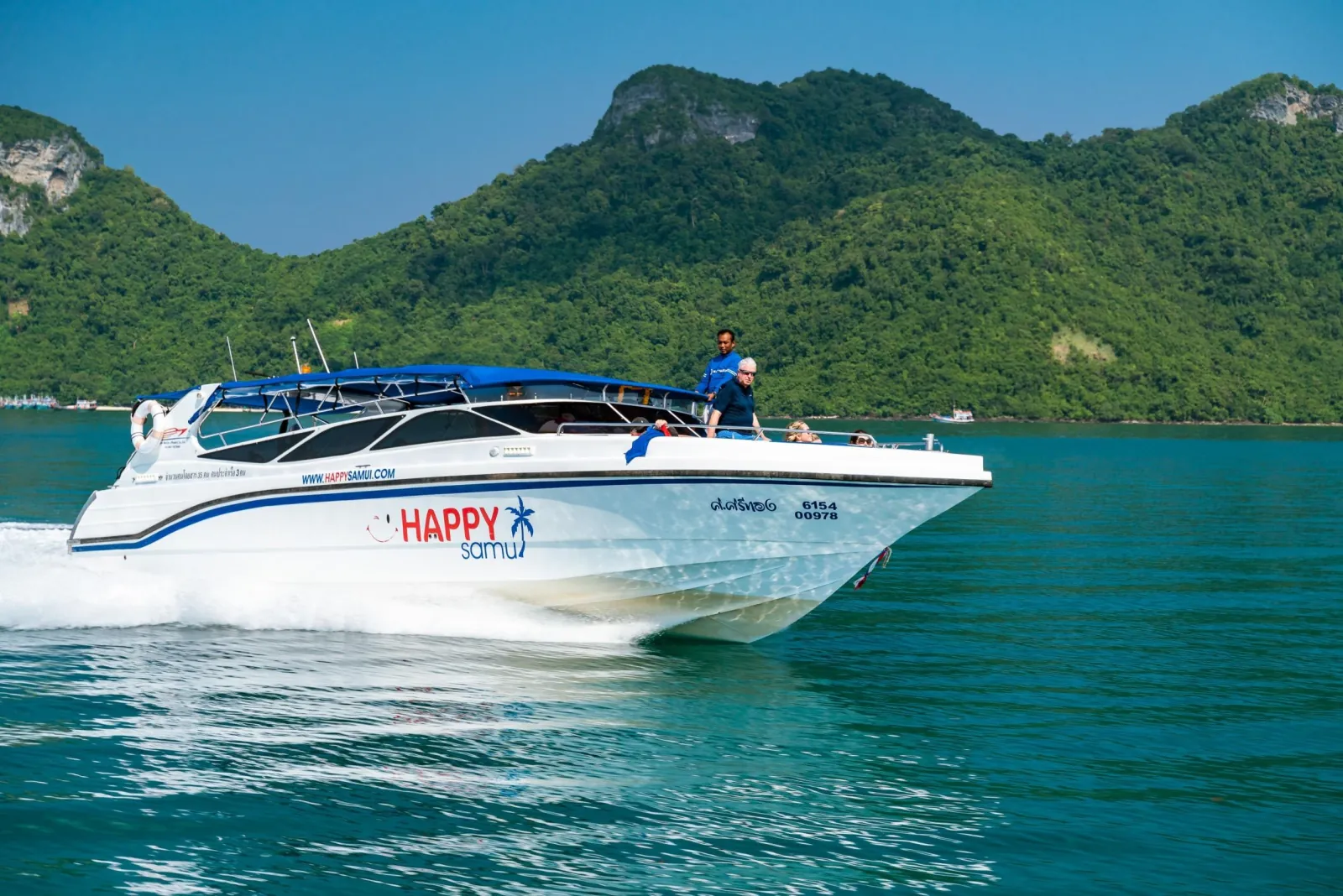 A white speedboat on flat water in front of a steep green headland