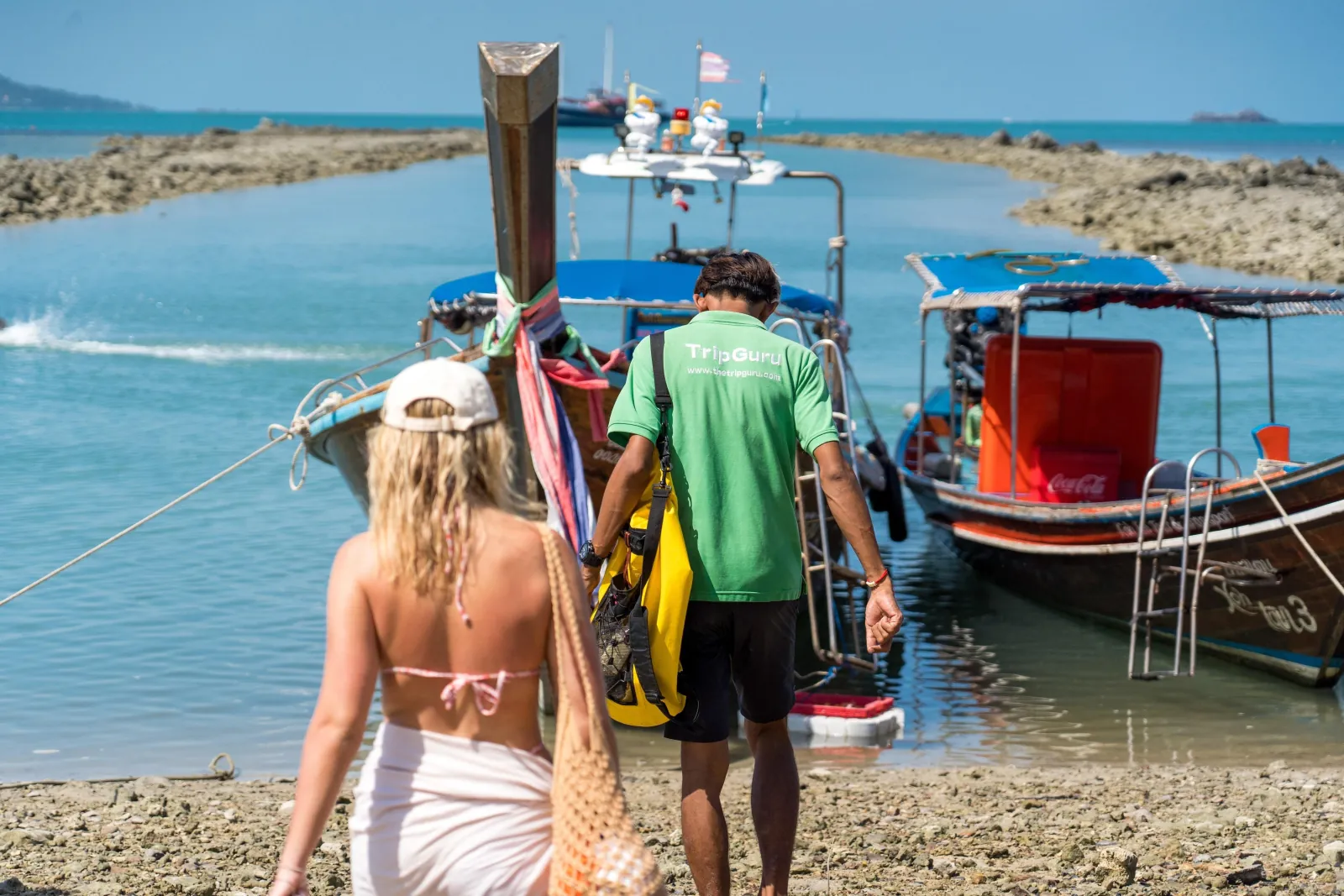 A guest walking down to a moored longtail while a guide loads snorkelling gear