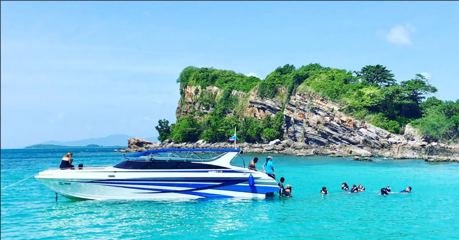 A speedboat moored off a rocky point with swimmers in the water alongside