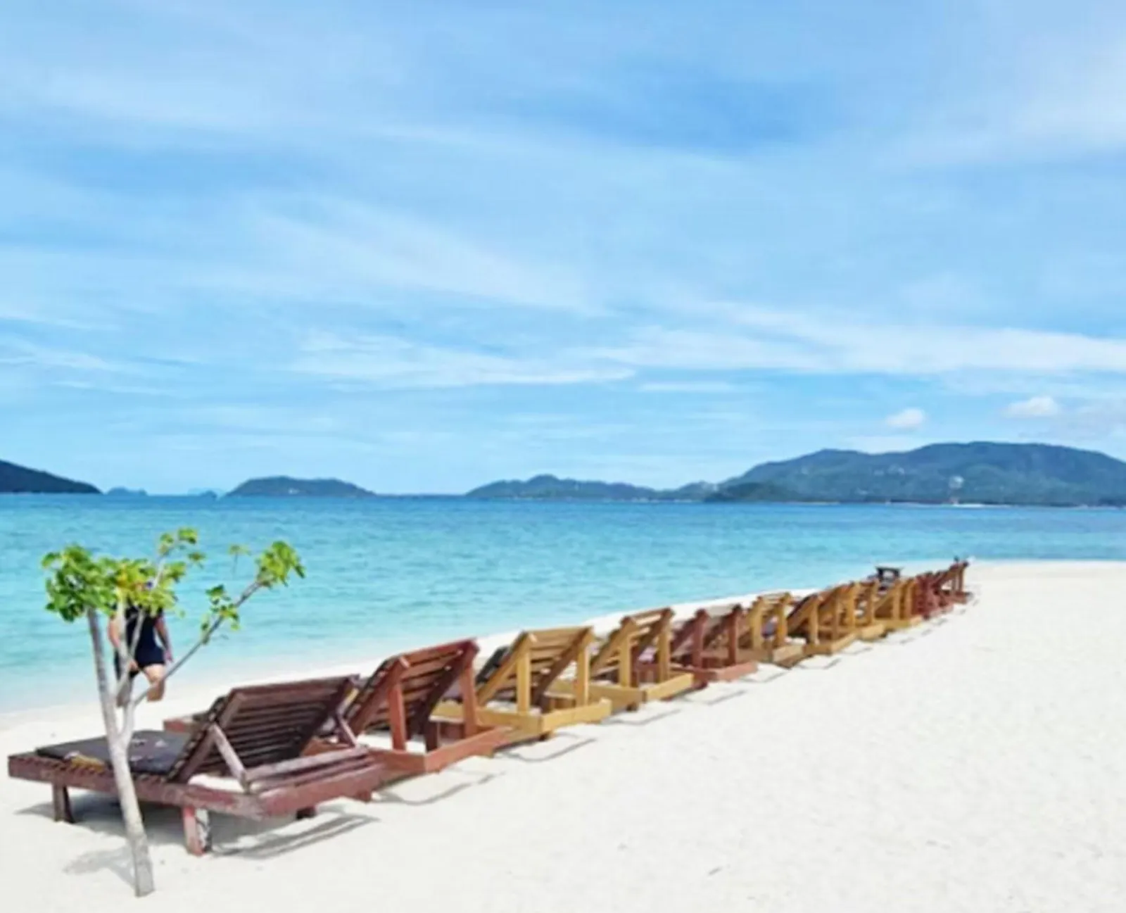 A line of wooden sun loungers along an empty stretch of white-sand beach