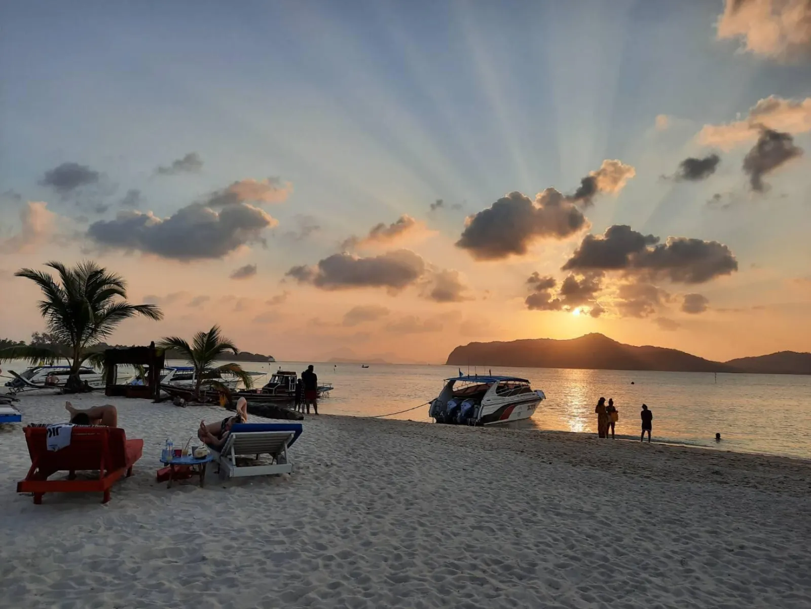 Sunset over the sea from the beach, with a speedboat drawn up on the sand