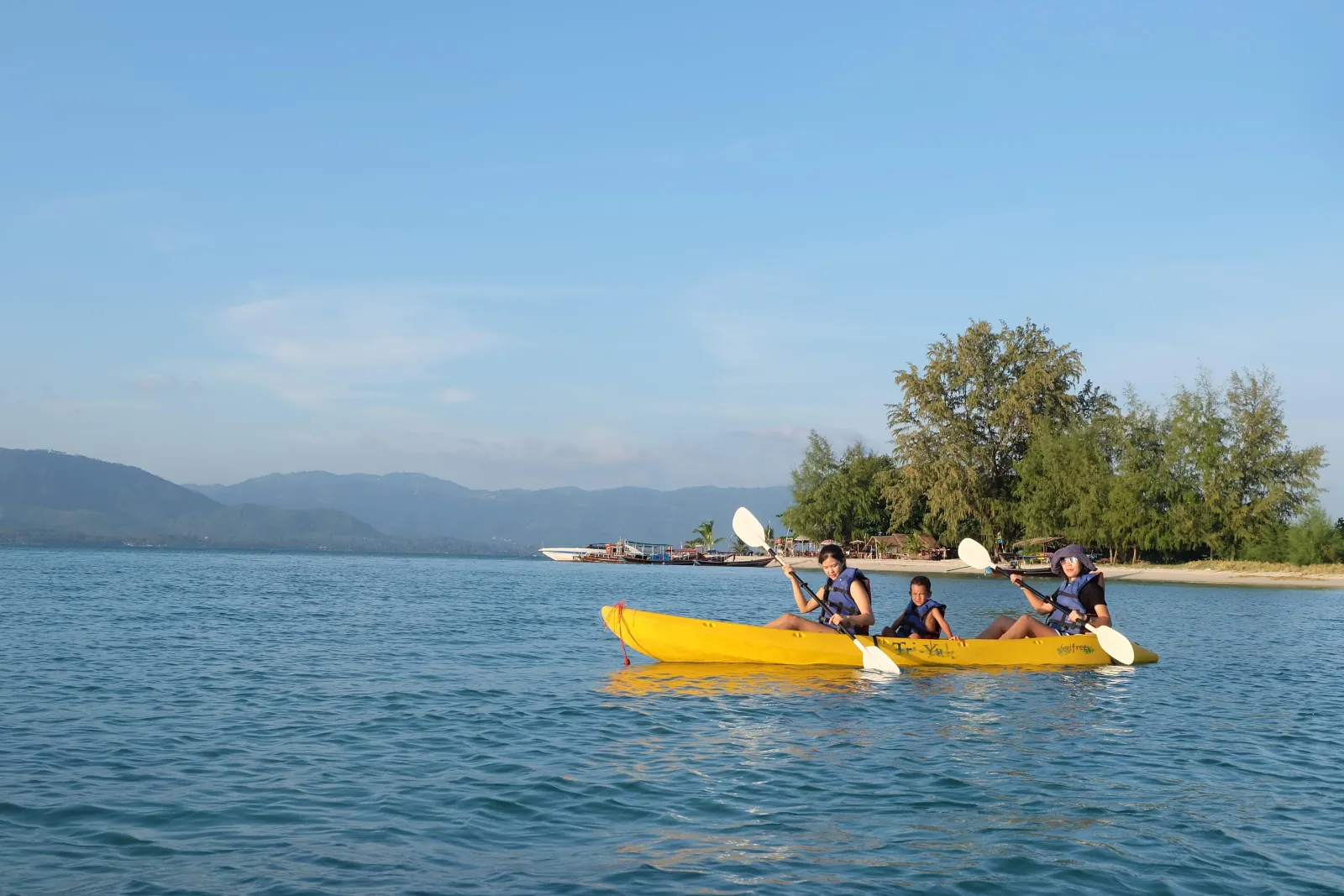 Guests paddling a yellow kayak along a tree-lined shore